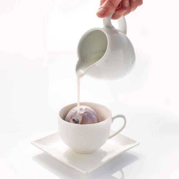 Hot chocolate bombe in a cup with milk pouring from a jug.