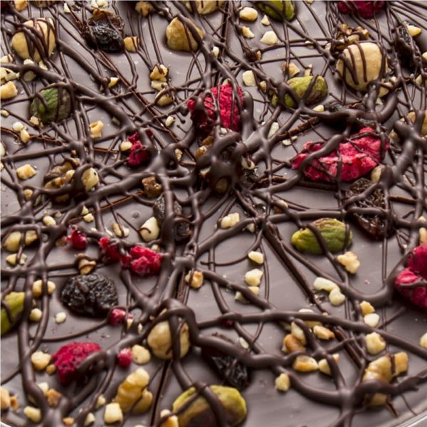 close up of dark chocolate pizza with fruit and nut on top